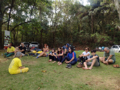 Pessoas de diversas idades reunidas em uma praça. Elas estão sentadas na grama e conversam entre si